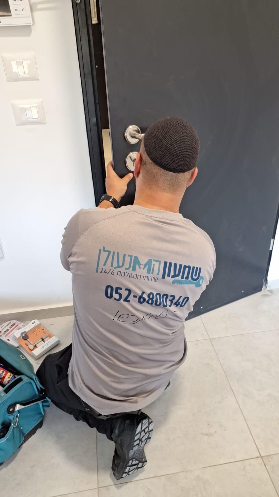 שמעון המנעולן מחליף צילינדר בדלת פלדלת, עם תיק כלים וצילינדר חדש באריזתו
